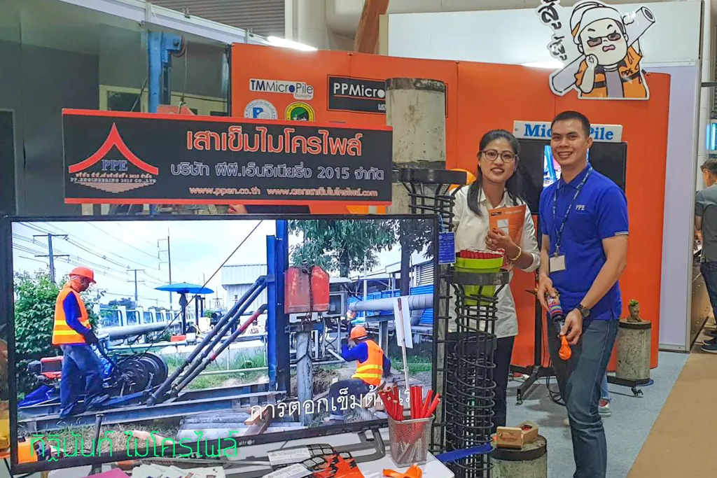 ผู้ร่วมออกบูธสองคนยืนข้างตัวอย่างเสาเข็มและโครงเหล็ก