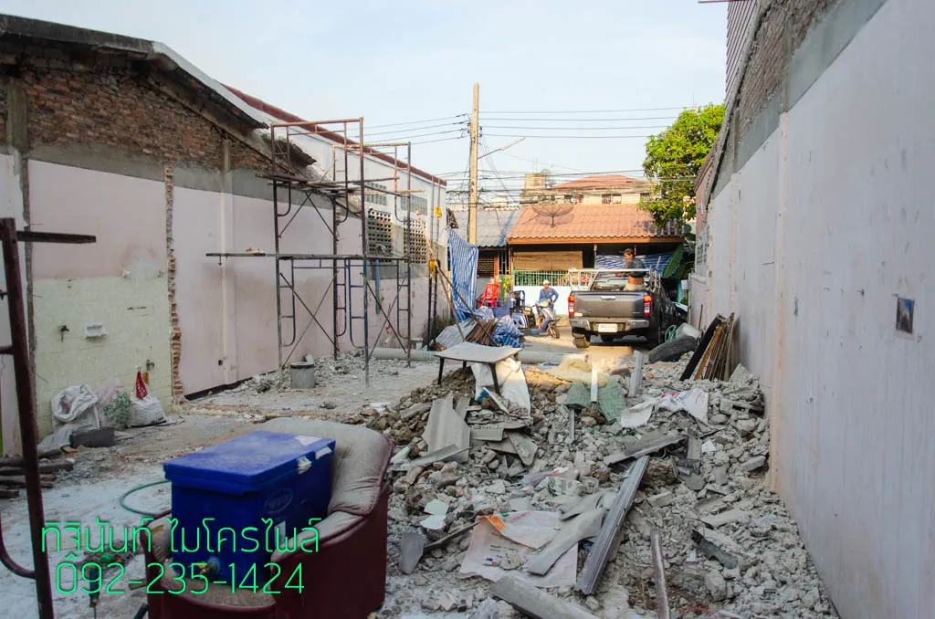 ทางเข้าพื้นที่ก่อสร้างที่มีเศษรื้อถอนและอาคารชุมชนอยู่ด้านนอก