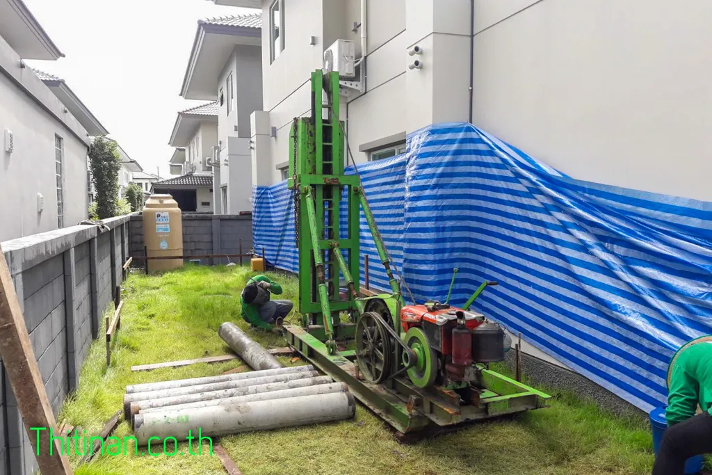 ปั้นจั่นไมโครไพล์และท่อนเสาเข็มในช่องข้างบ้านที่มีผ้าใบคลุมผนัง